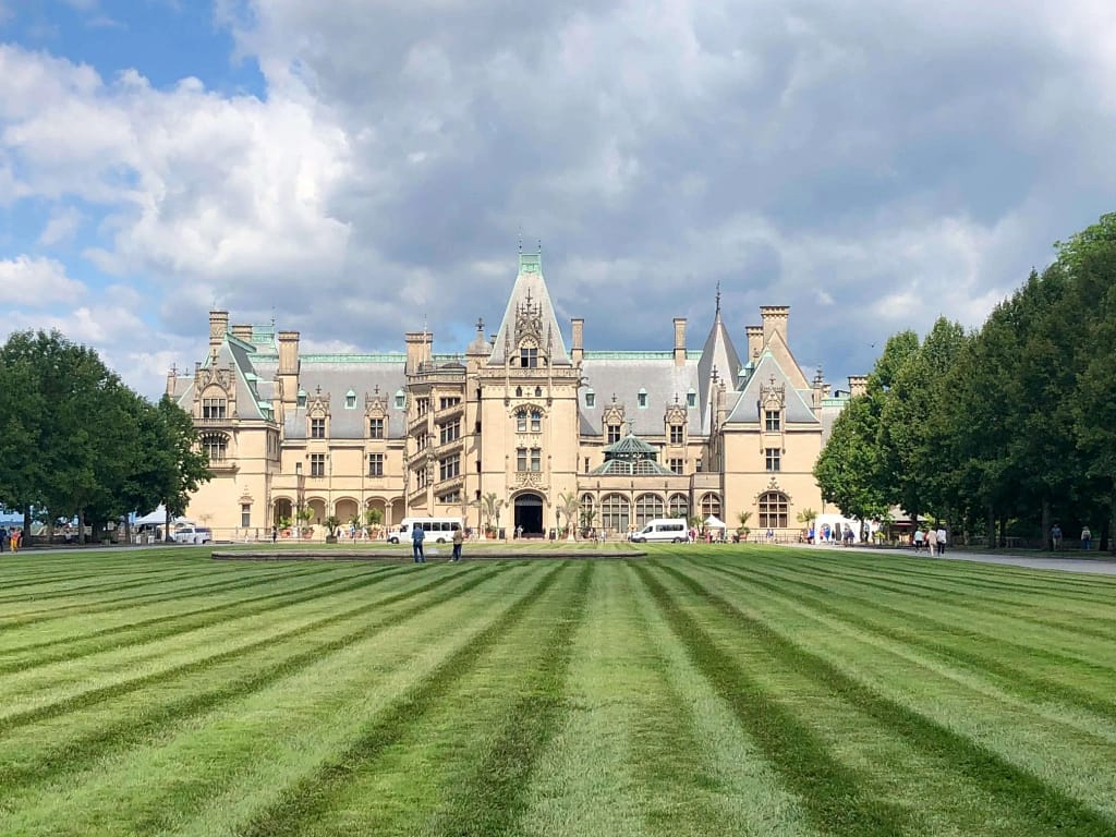 a large building with a lawn and trees with Biltmore Estate in the background